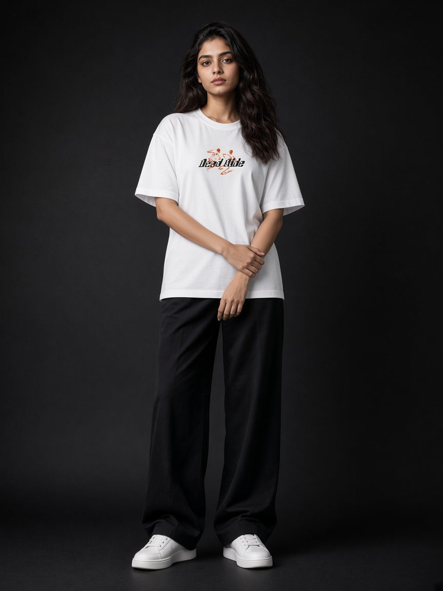 A woman modeling a white short-sleeve graphic T-shirt with 'I'm Not A Liar' printed in black script with small orange and red graphic elements, paired with black wide-leg pants and white sneakers, set against a dark studio background.
