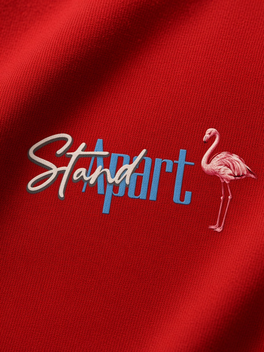 A close-up of a red textured fabric featuring an embroidered design with the words 'Stand Apart' in white and blue, alongside a pink flamingo.